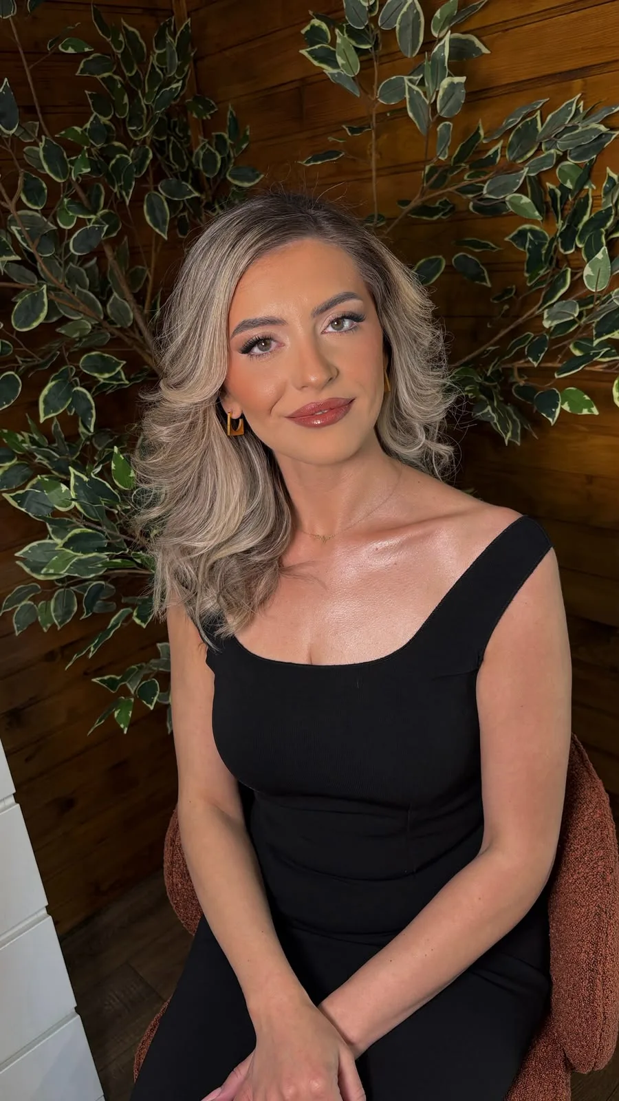 Machiaj luminos pe o clientă blondă, cu părul ondulat, lângă un ficus decorativ